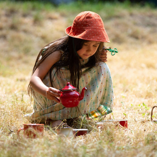 Child plating with a tea set in a grass field wearing Cherries Reversible Sunhat in Olive
