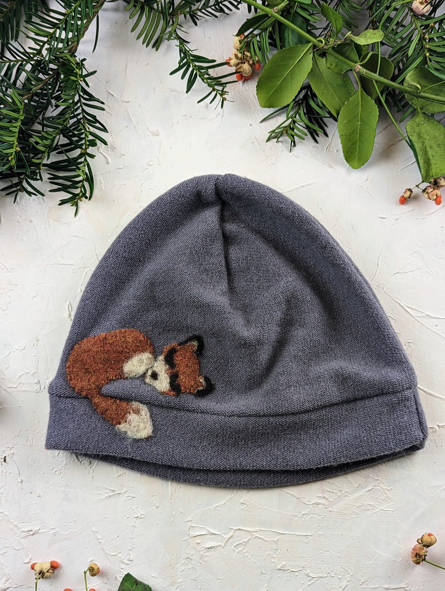 Gray beanie with a fox patch on a light background with greenery