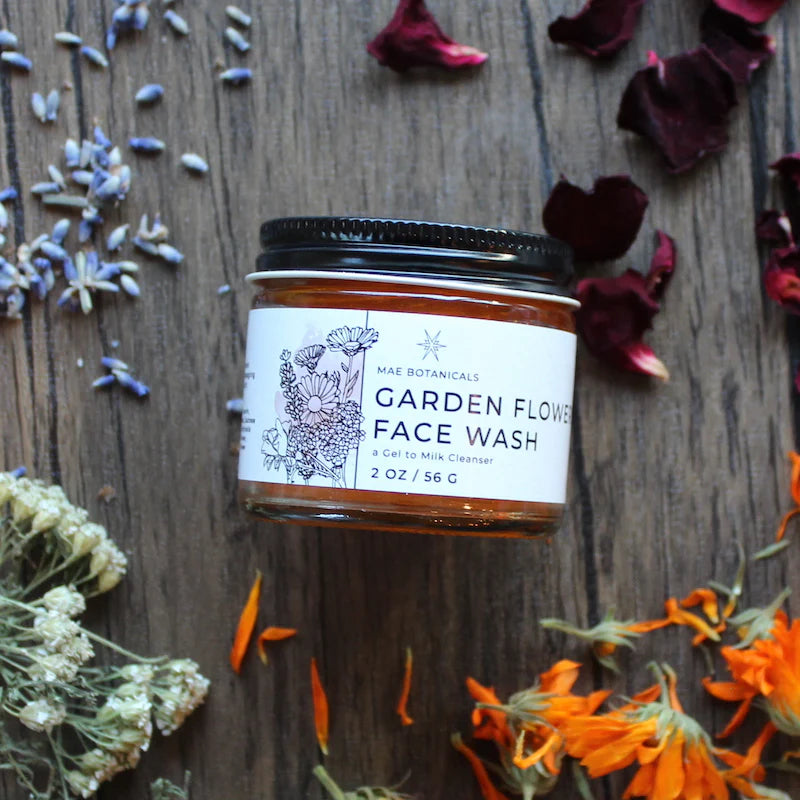 2 oz jar of garden flower faec wash on a wooden table surrounded by flower petals