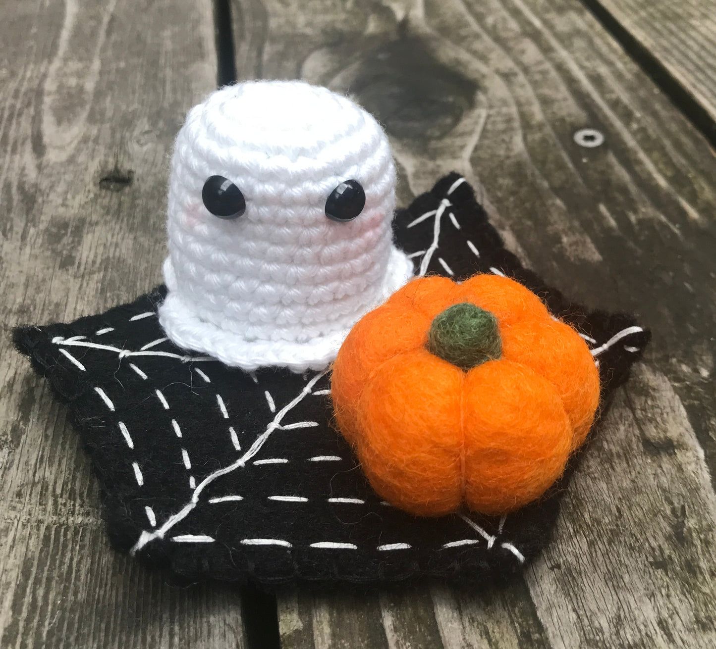 Crocheted ghost with a small pumpkin on a felt spider web