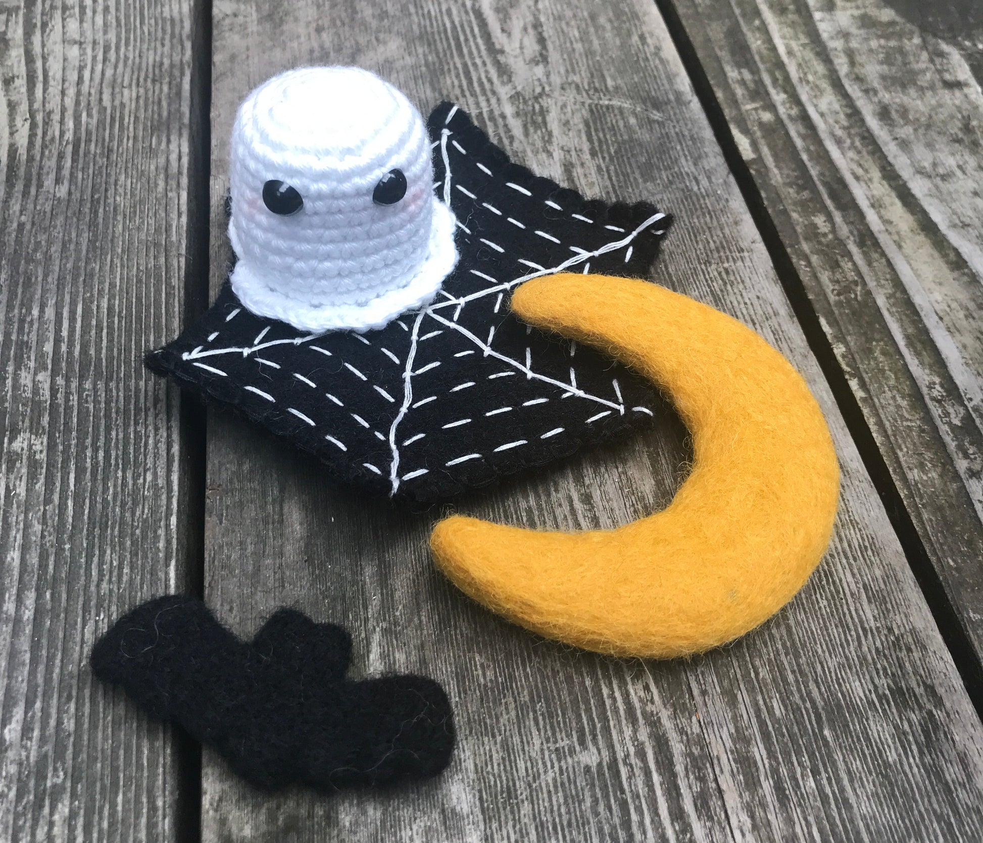 Decorative scene with a crochet ghost, felt moon, spider web, and black bat on a wooden surface