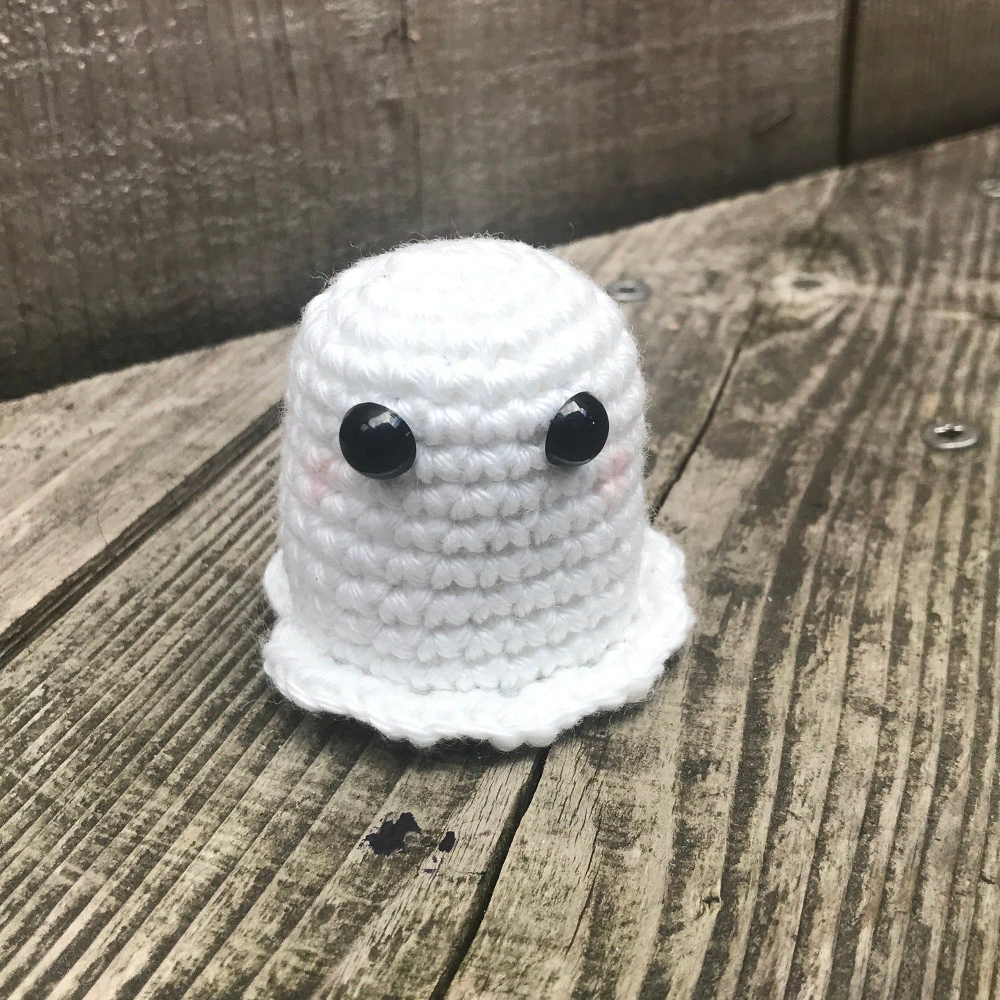 Small white crocheted ghost toy with black button eyes on a wooden surface