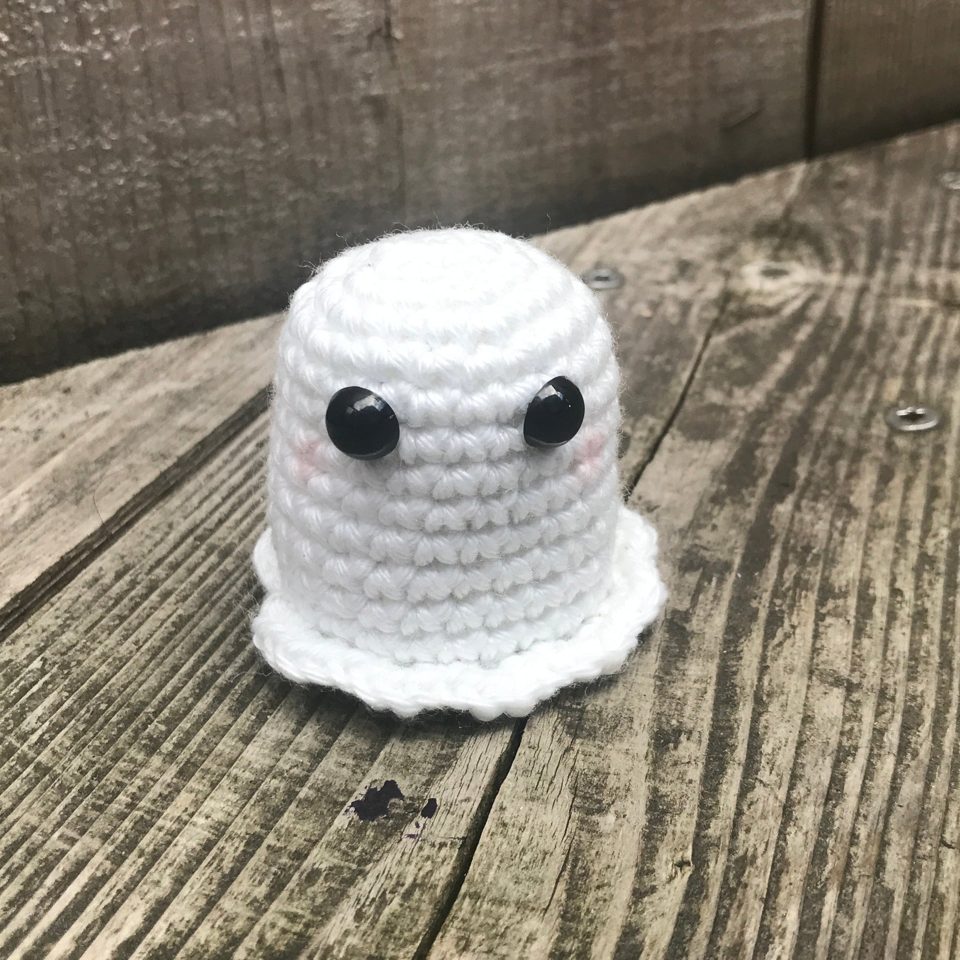 Small white crocheted ghost toy with black button eyes on a wooden surface