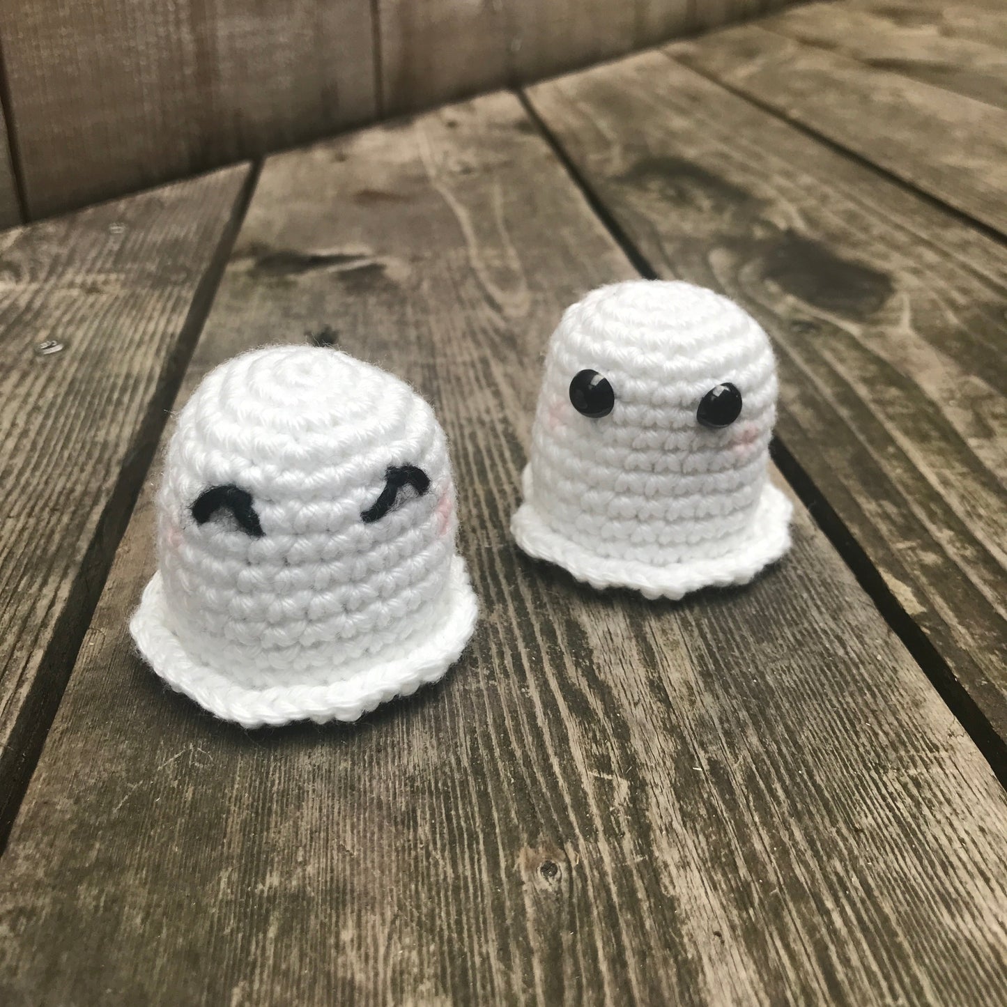Two white crocheted ghost toys on a wooden surface