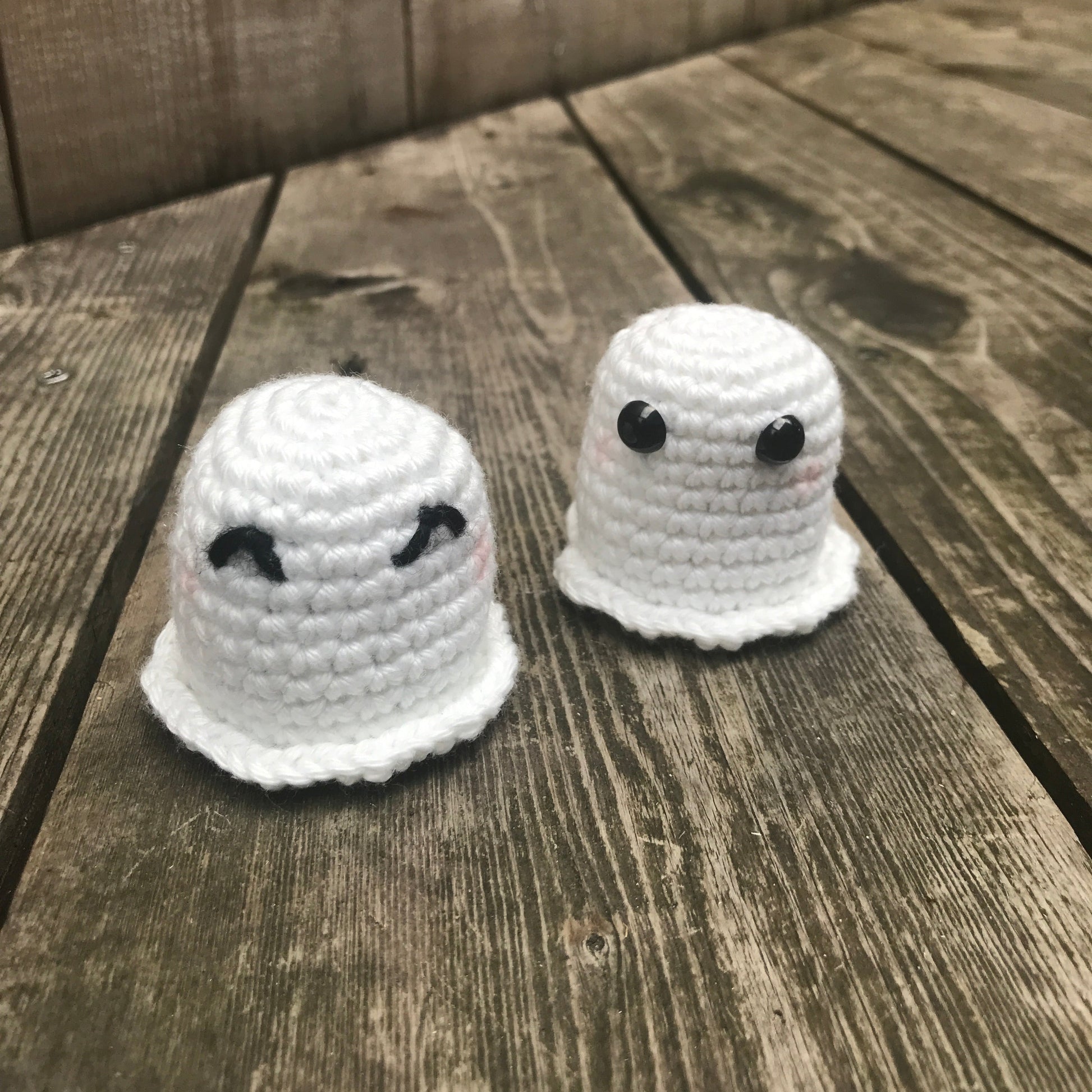 Two white crocheted ghost toys on a wooden surface