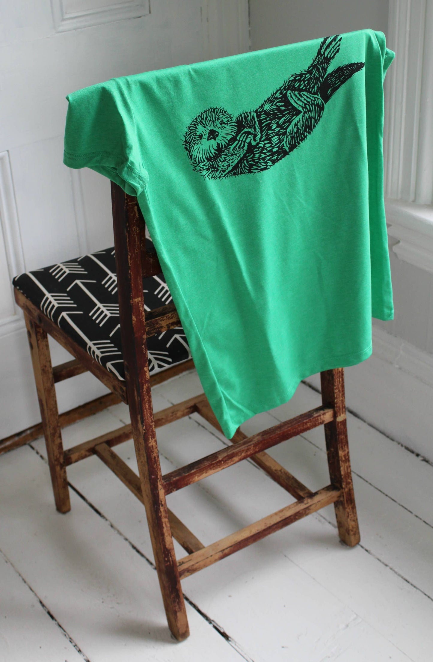 Green towel with a black otter design draped over a wooden chair.