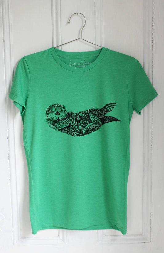 Green t-shirt with a black otter design on a white wooden panel background