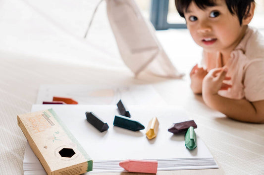 child laying on the floor drawing with triangle beeswax crayons