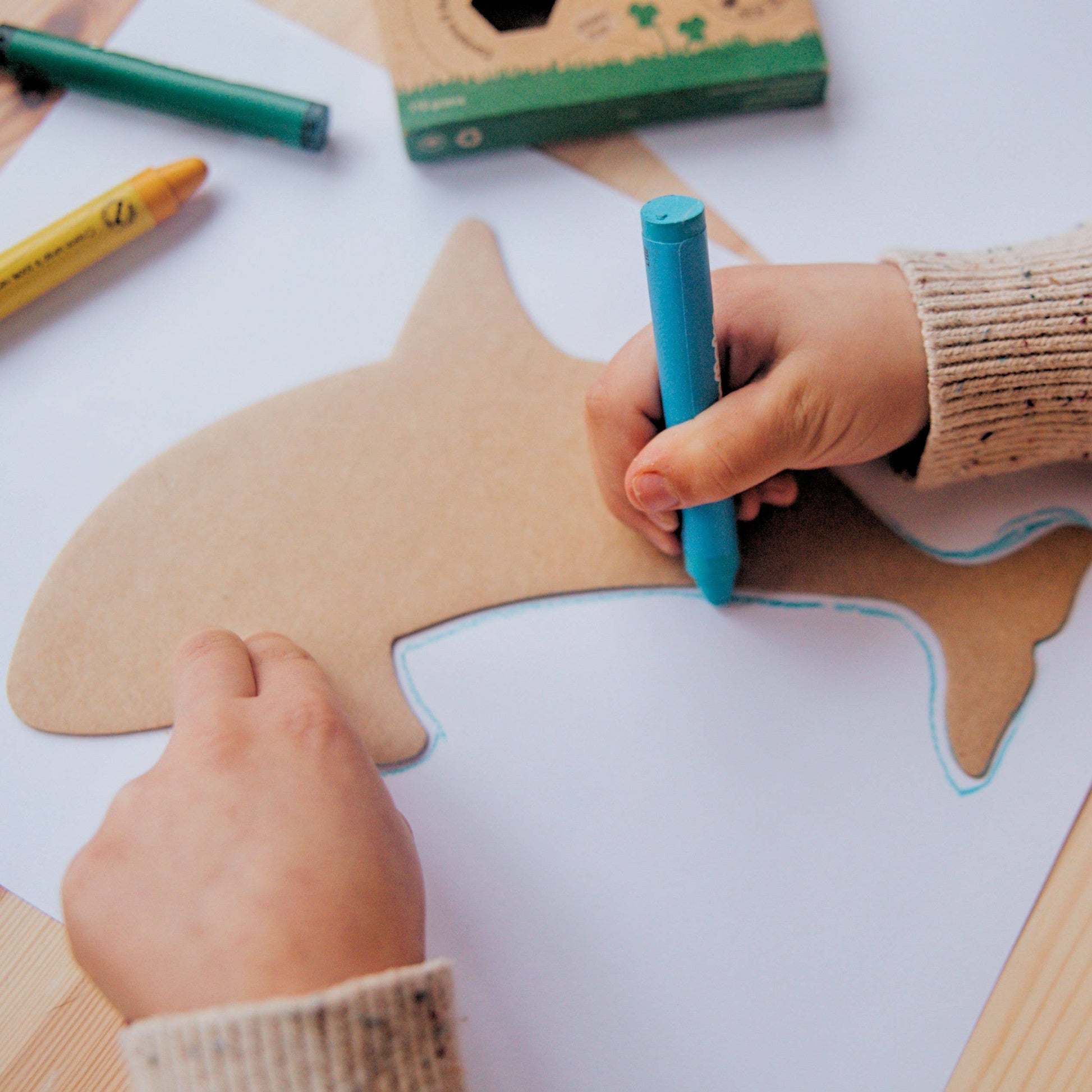 Close up of a child's hands drawing a dolphin with a cardboard stencils and crayons