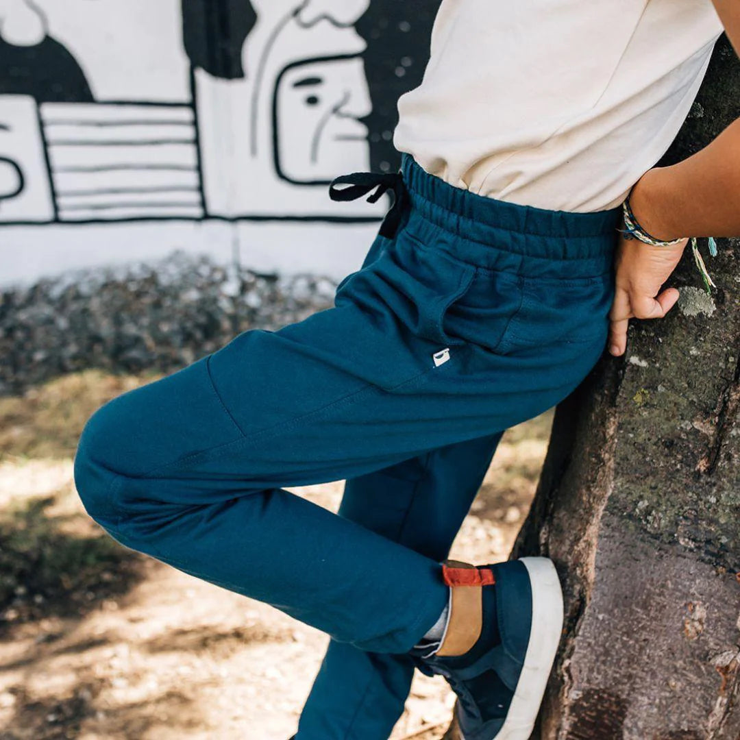 child leaning against a tree wearing kay sweatpants in peacock blue