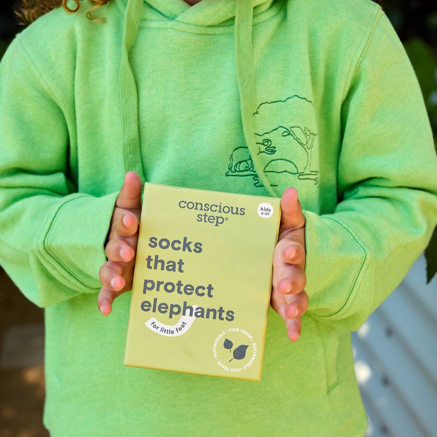 Person wearing a green hoodie holding a 'Conscious Step' product packaging.