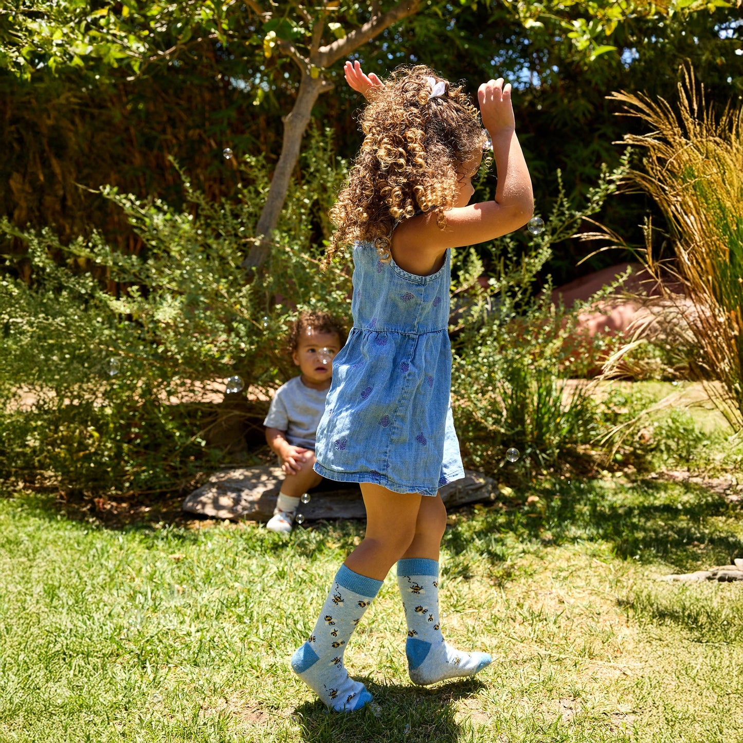 Child in a blue dress playing outdoors with greenery in the background