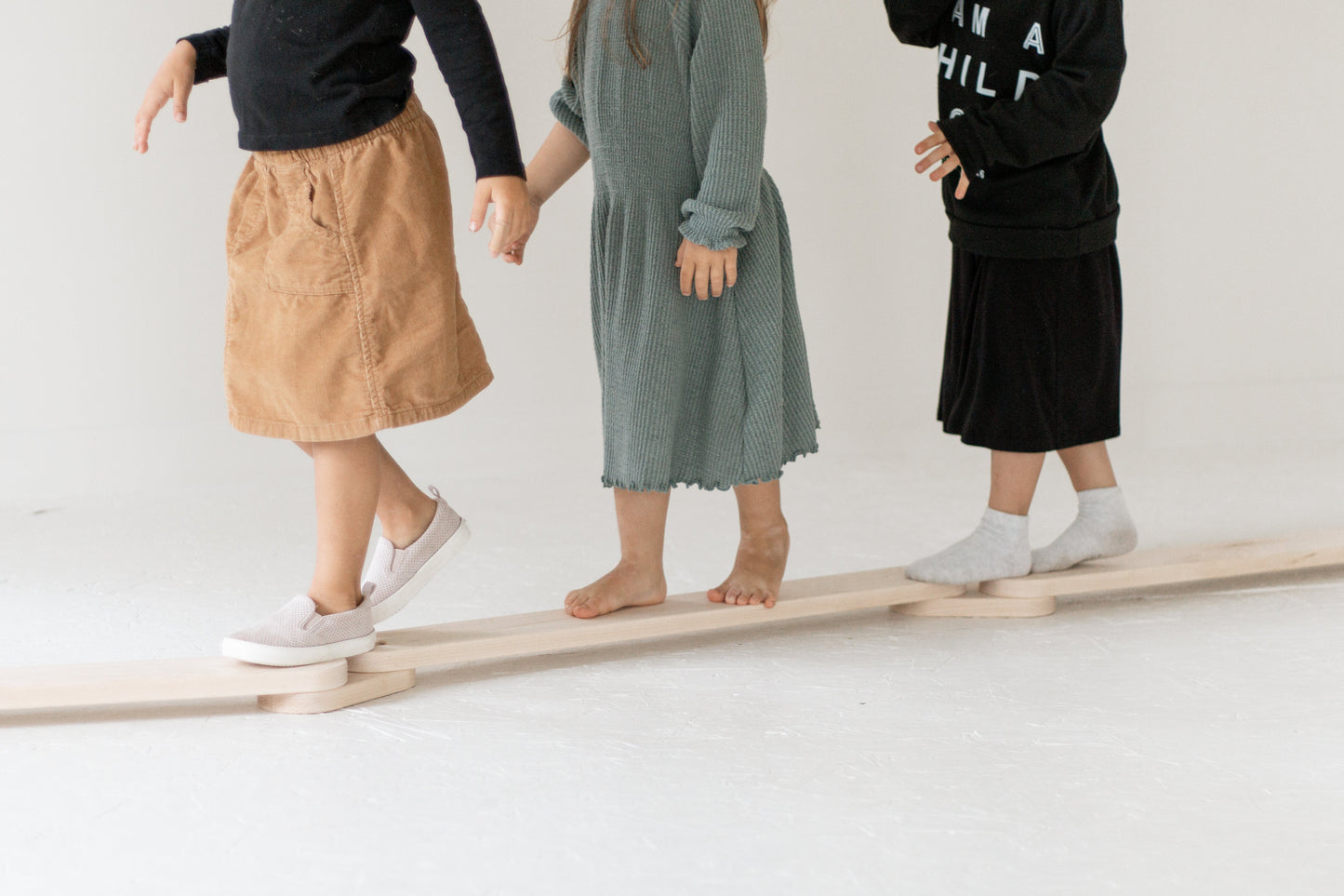 Three people standing on a wooden balance beam against a white background