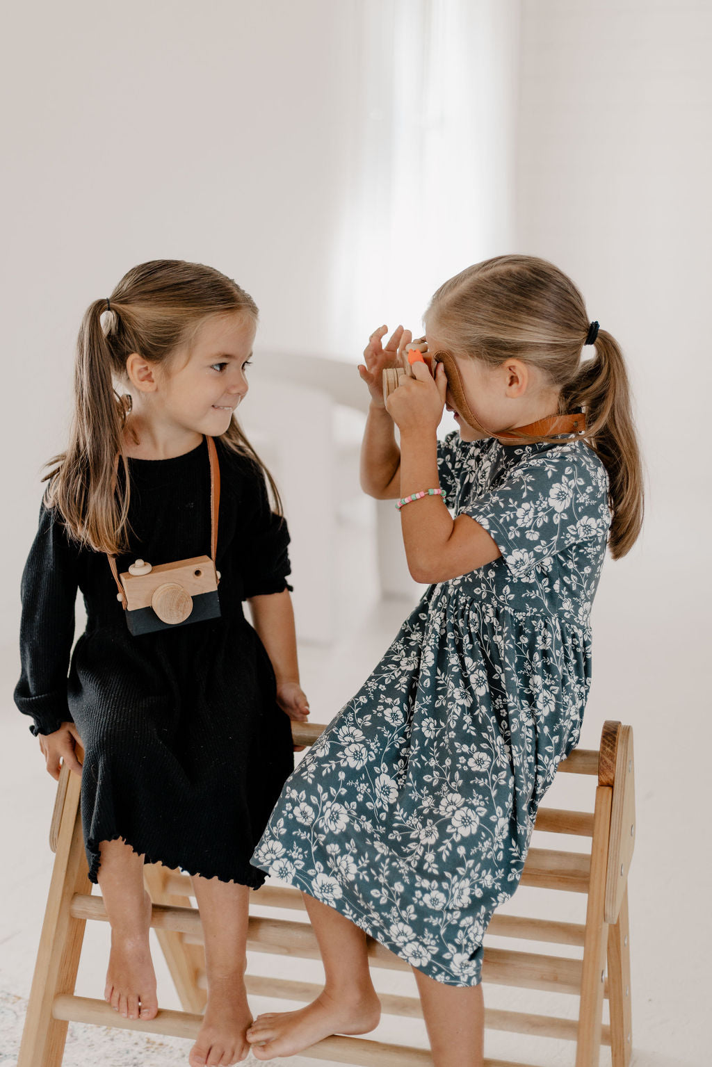 Two young girls playing with a toy camera indoors.