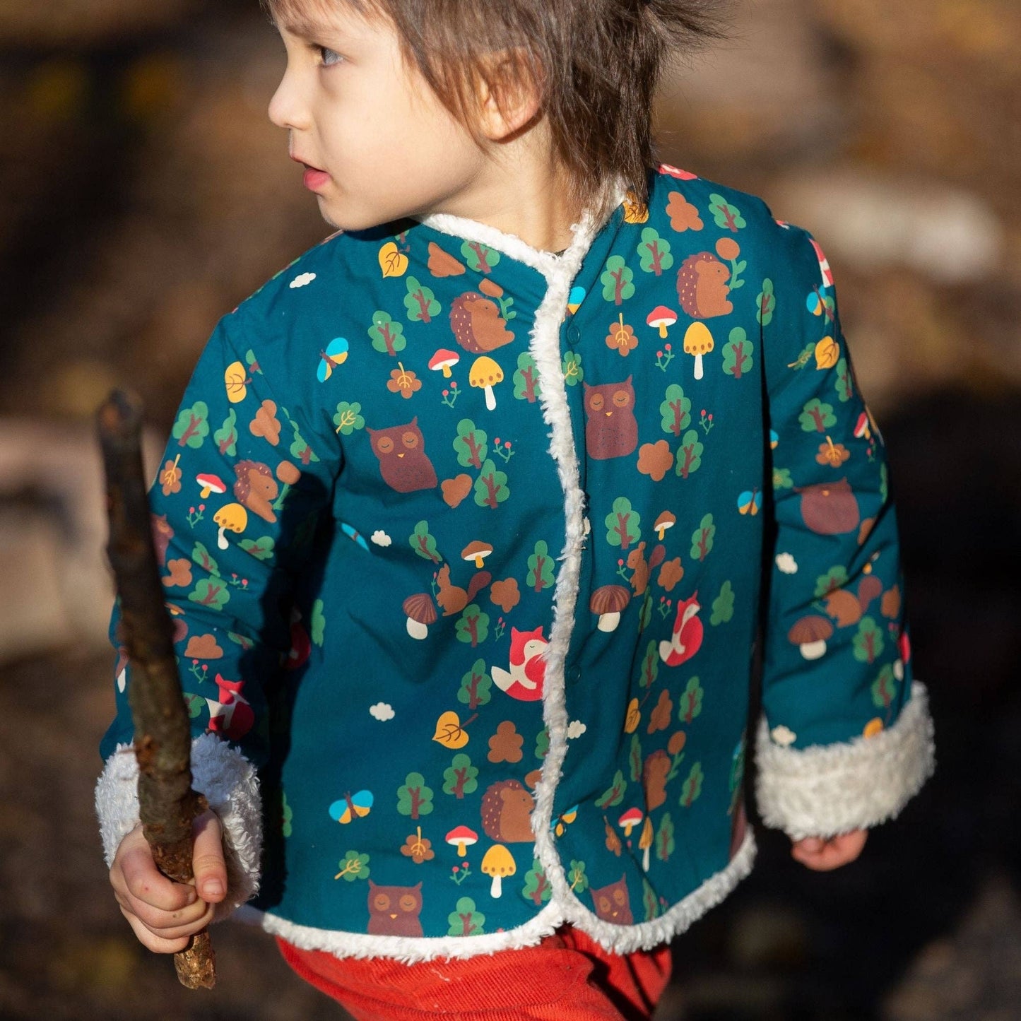 A child carrying a wooden stick wearing an enchanted forest reversible jacket