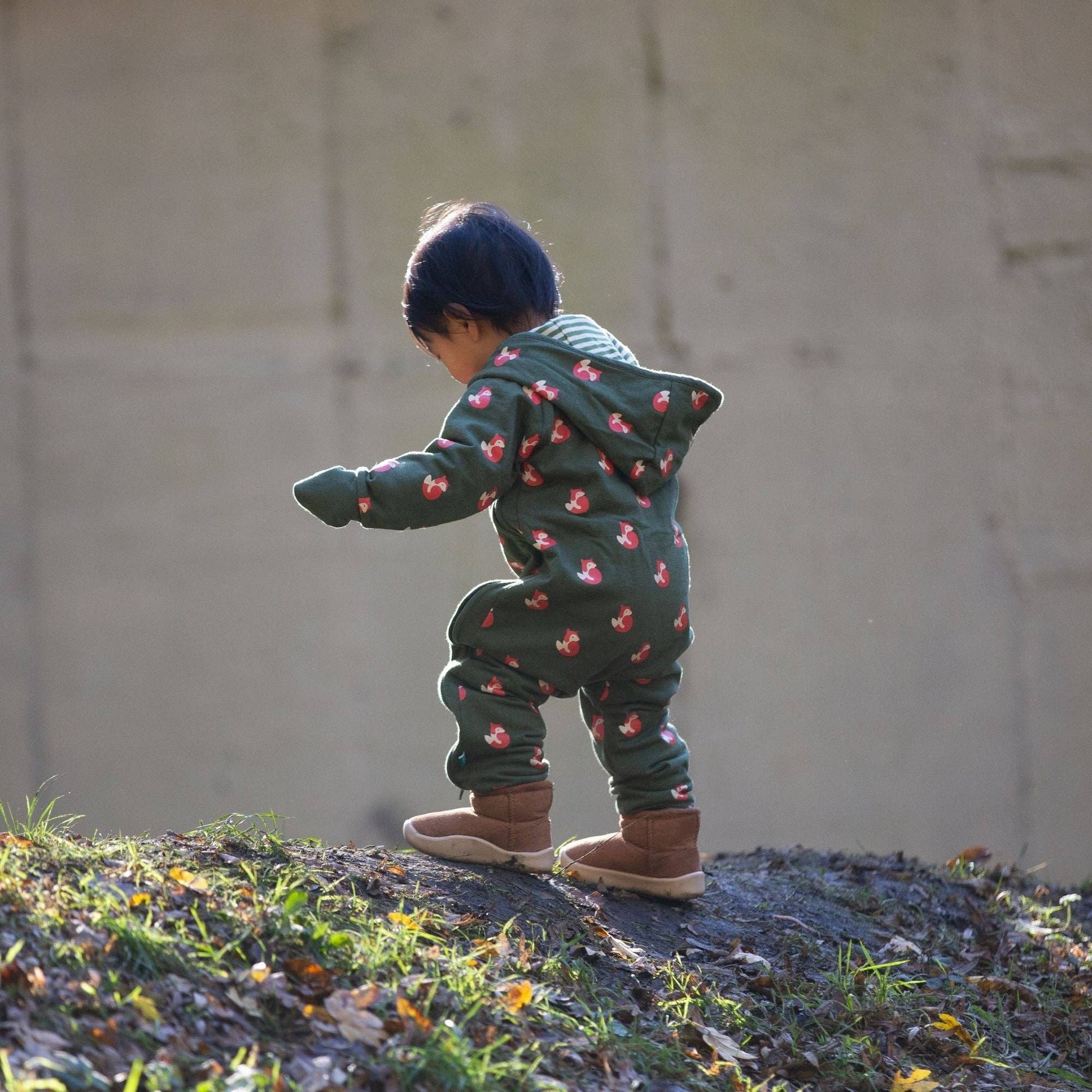 A toddler climbing a small hill wearing foxes snug as a bug suit