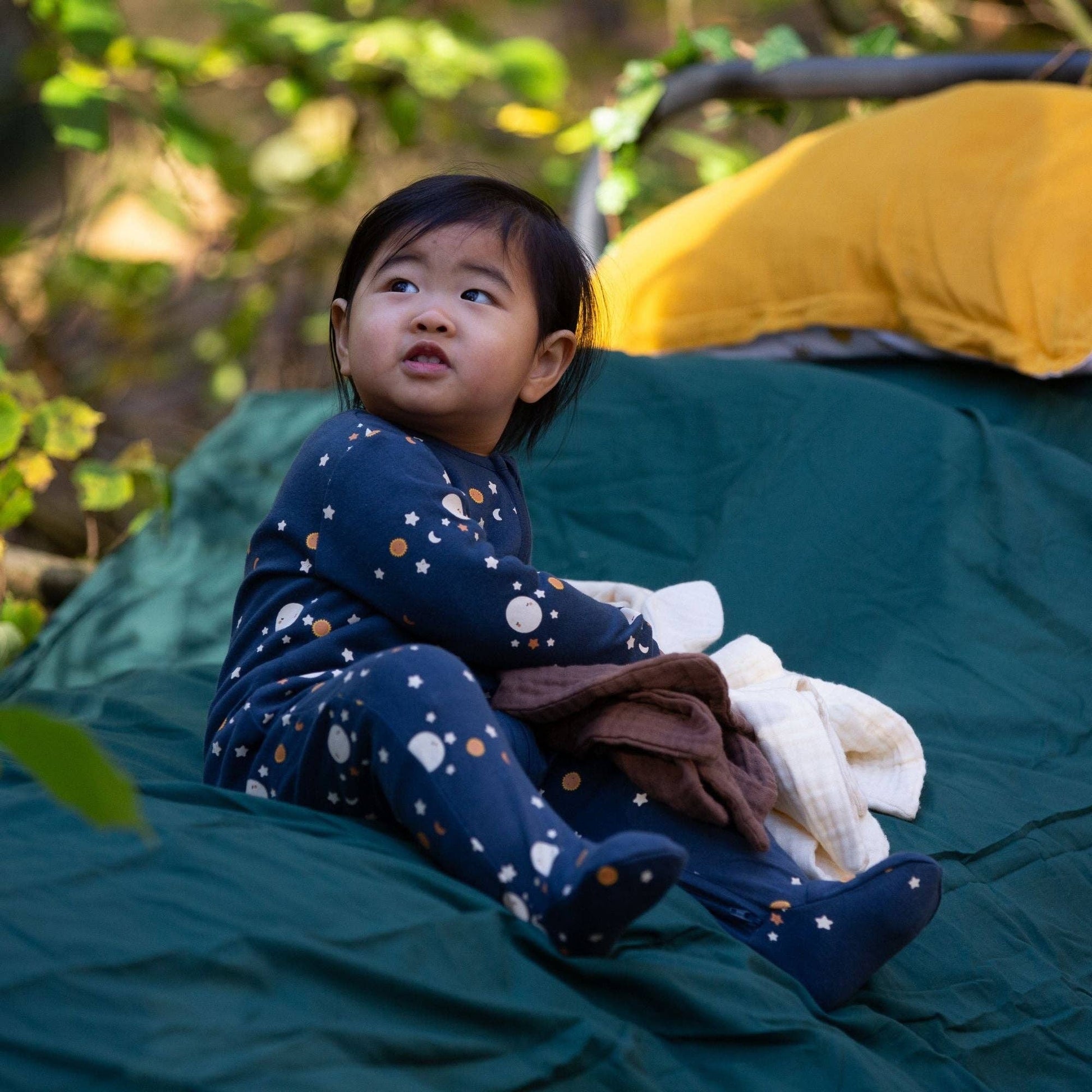 Baby wearing over the moon organic footie sitting outdoors on a blanket