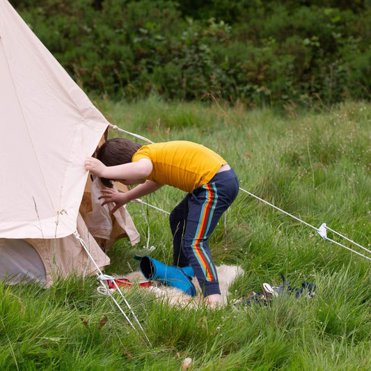 A child entering a camping tent wearing a yellow t-shirt and navy rainbow stripe joggers