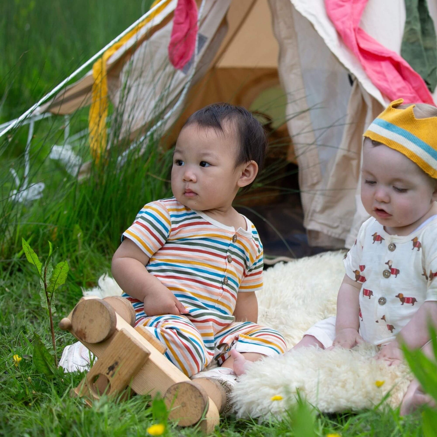 two babies sitting in the grass in front of a tent wearing organic summer rompers