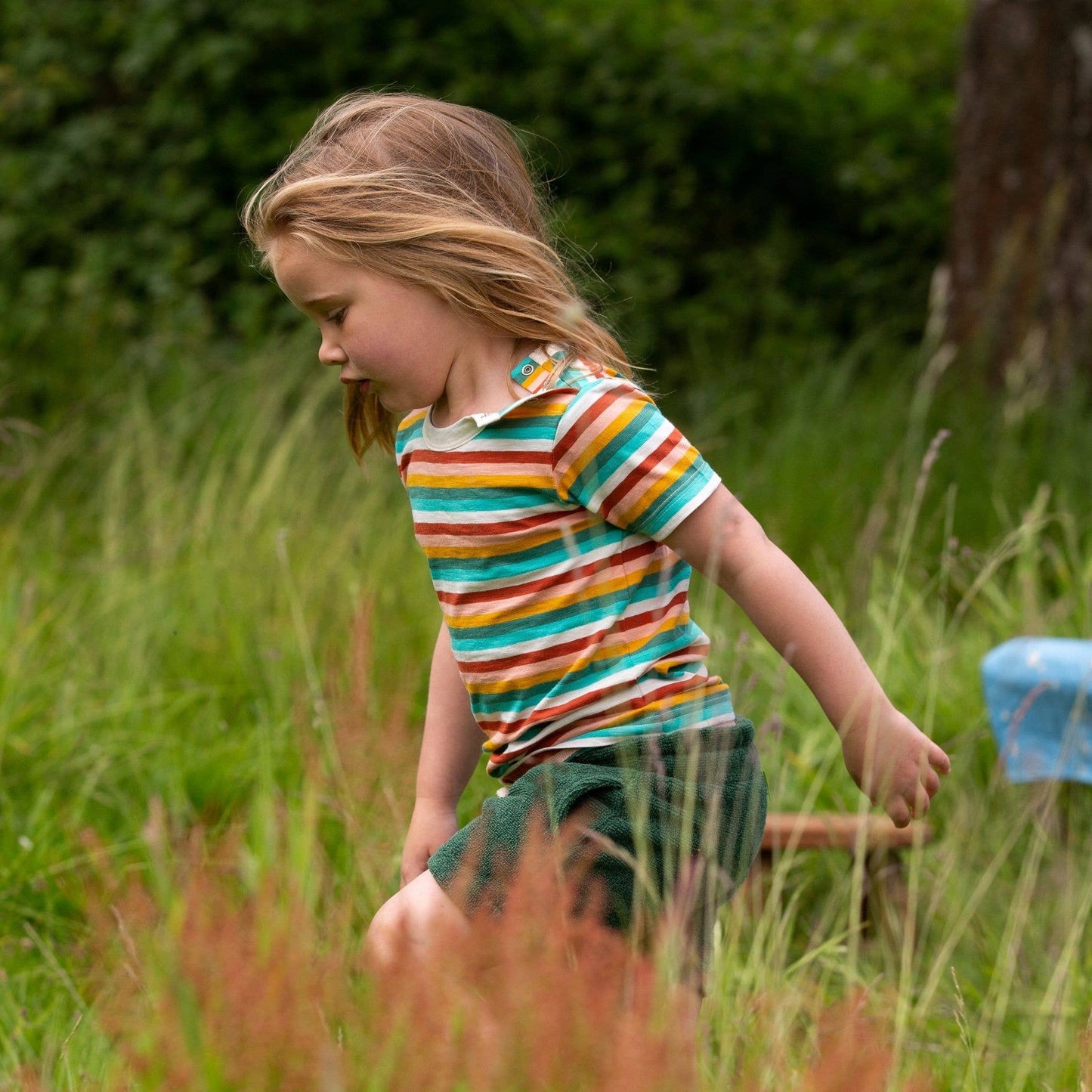 a child running in the grass wearing shorts and a rainbow striped short sleeve tee