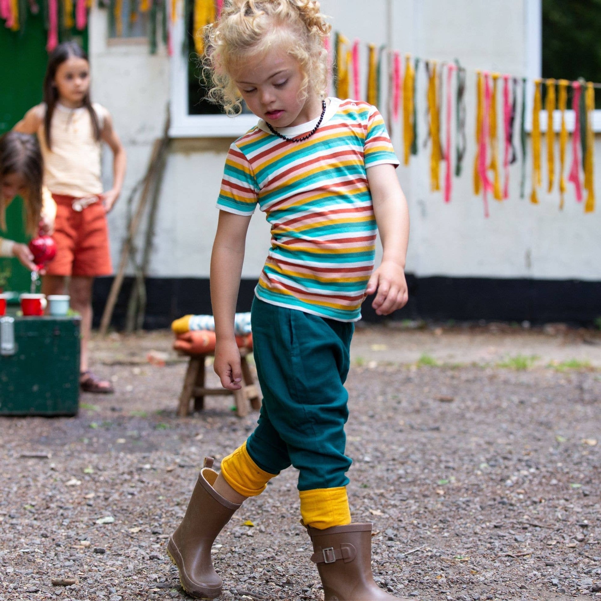 a child walking outside wearing blue pants and a rainbow organic short sleeve tee