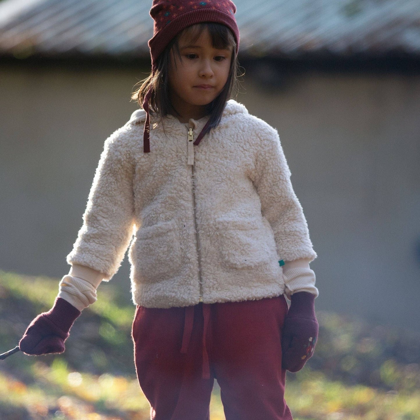 Child standing outside holding a stick wearing sherpa fleece campfire jacket