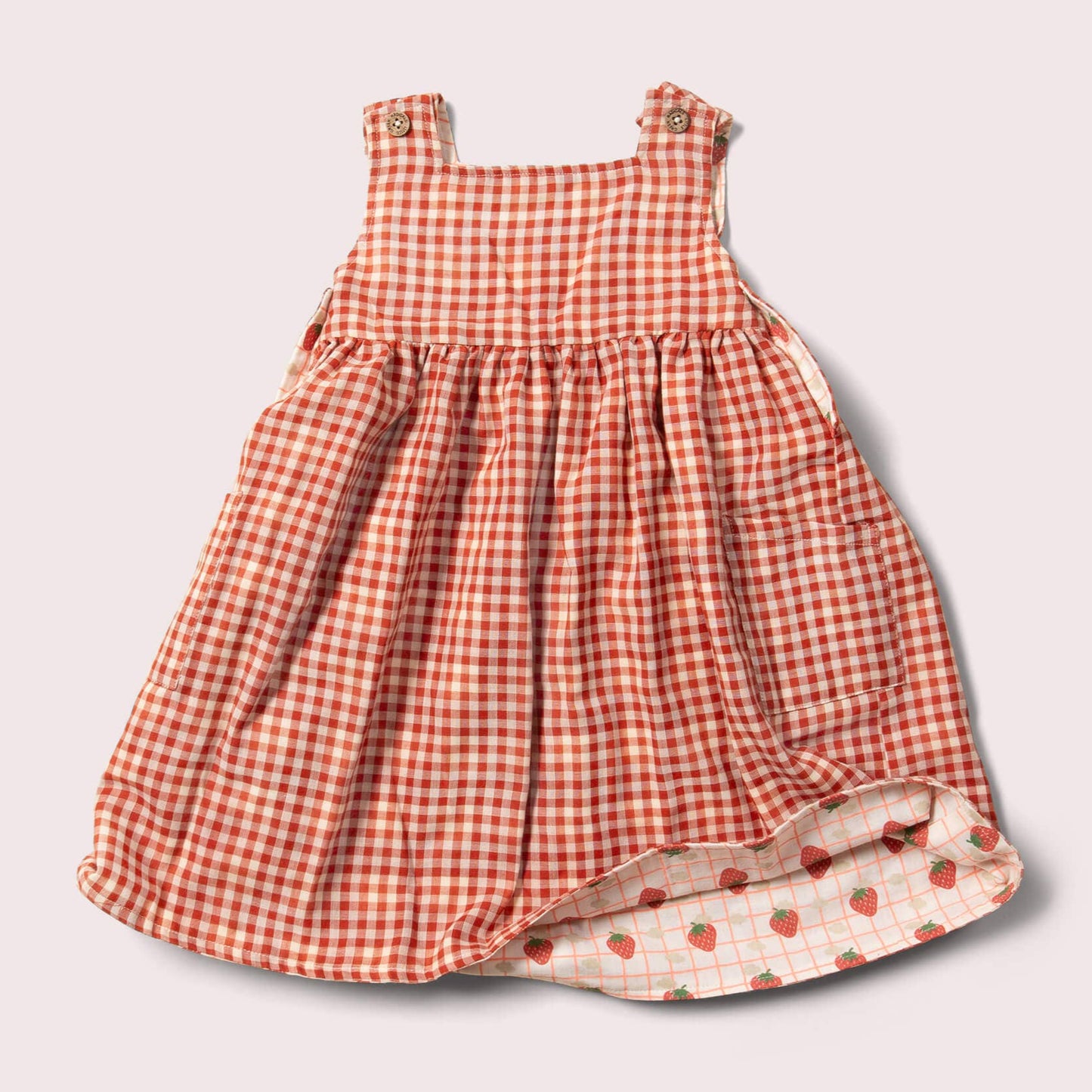 reversible strawberry pinny dress laid flat on the red checsk side