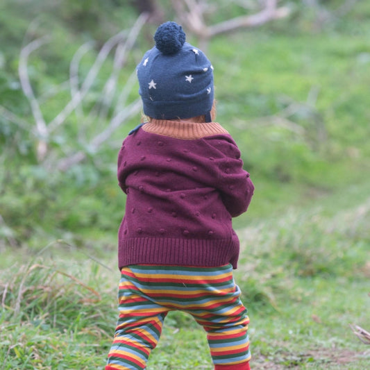 child walking outside wearing a hat, sweater, and rainbow striped joggers