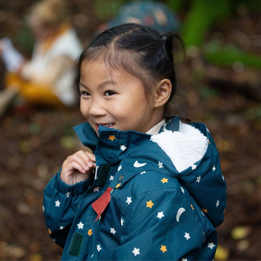 A child standing in the woods wearing a moon and stars waterproof recycled winter coat