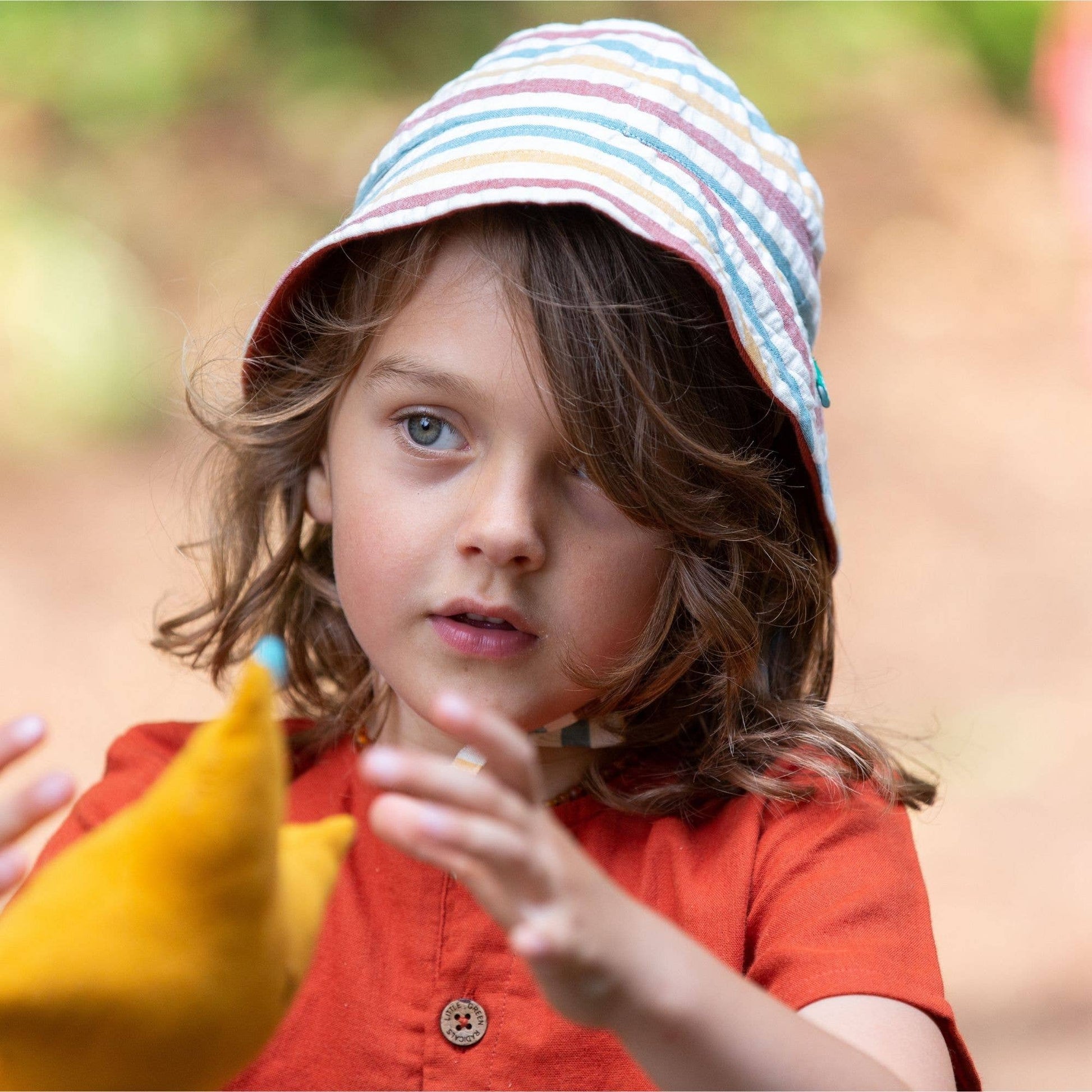 child holding a toy wearing an orange shirt and reversible striped sunhat