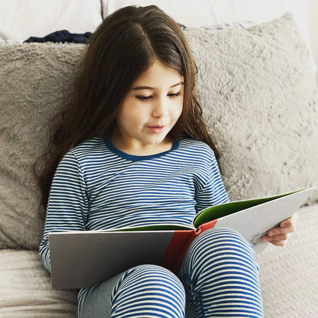 Child with long hair reading a book wearing blue stripes wool silk long underwear