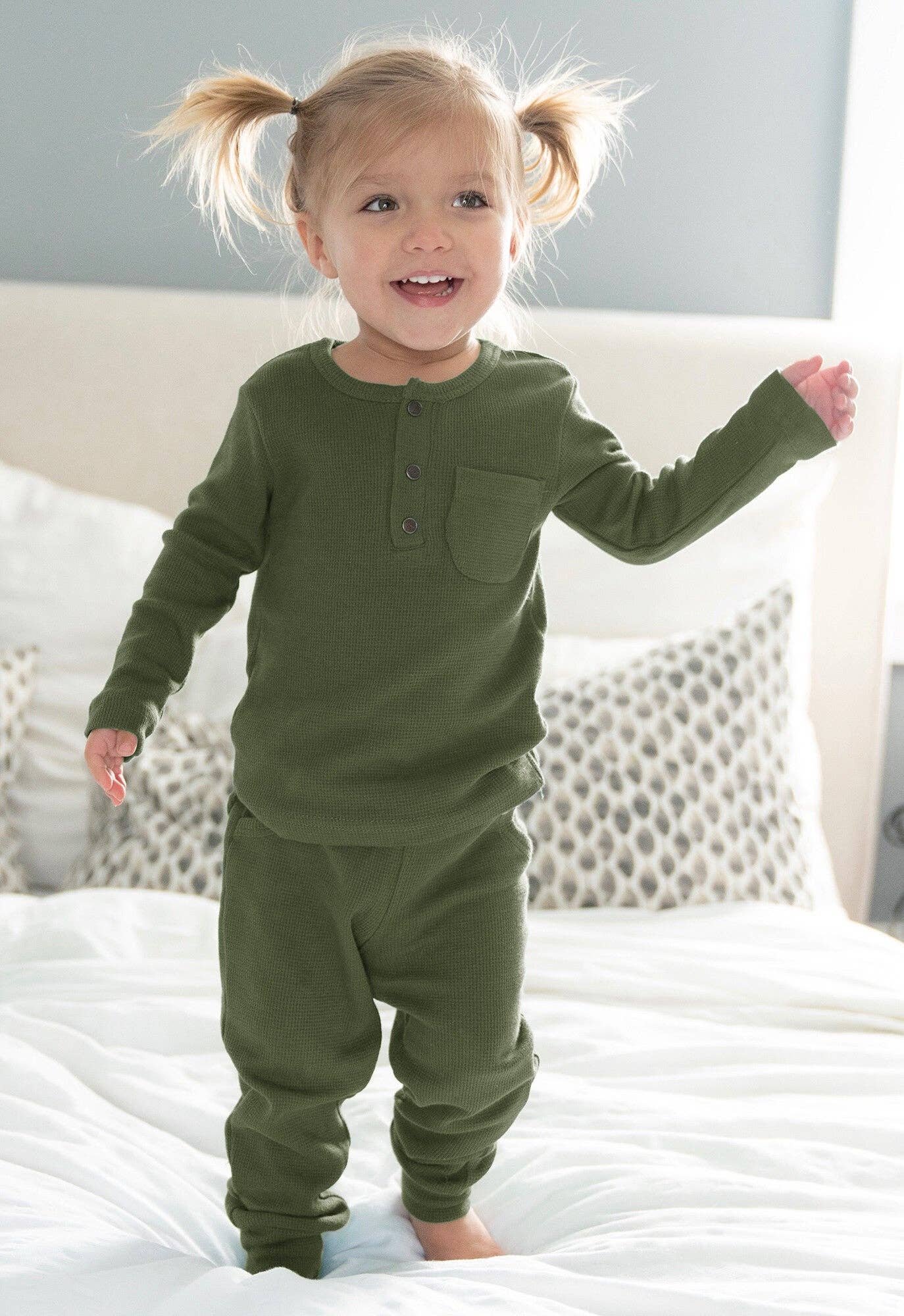 Child wearing green thermal pajamas standing on a bed