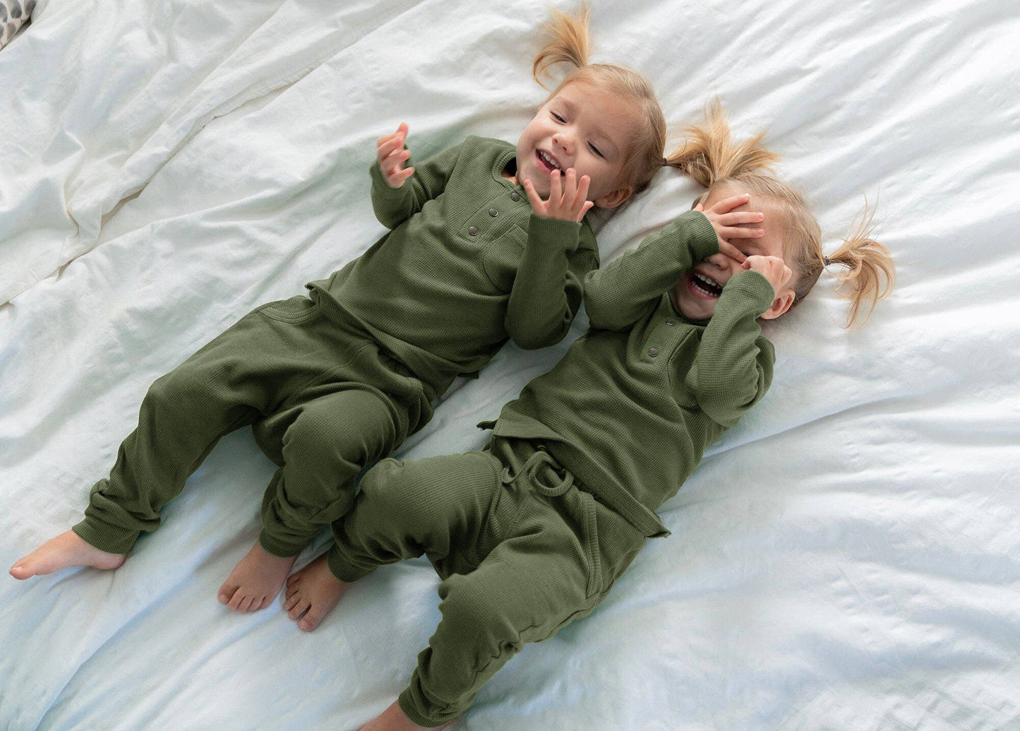 Two children in green thermal pajamas lying on a white blanket