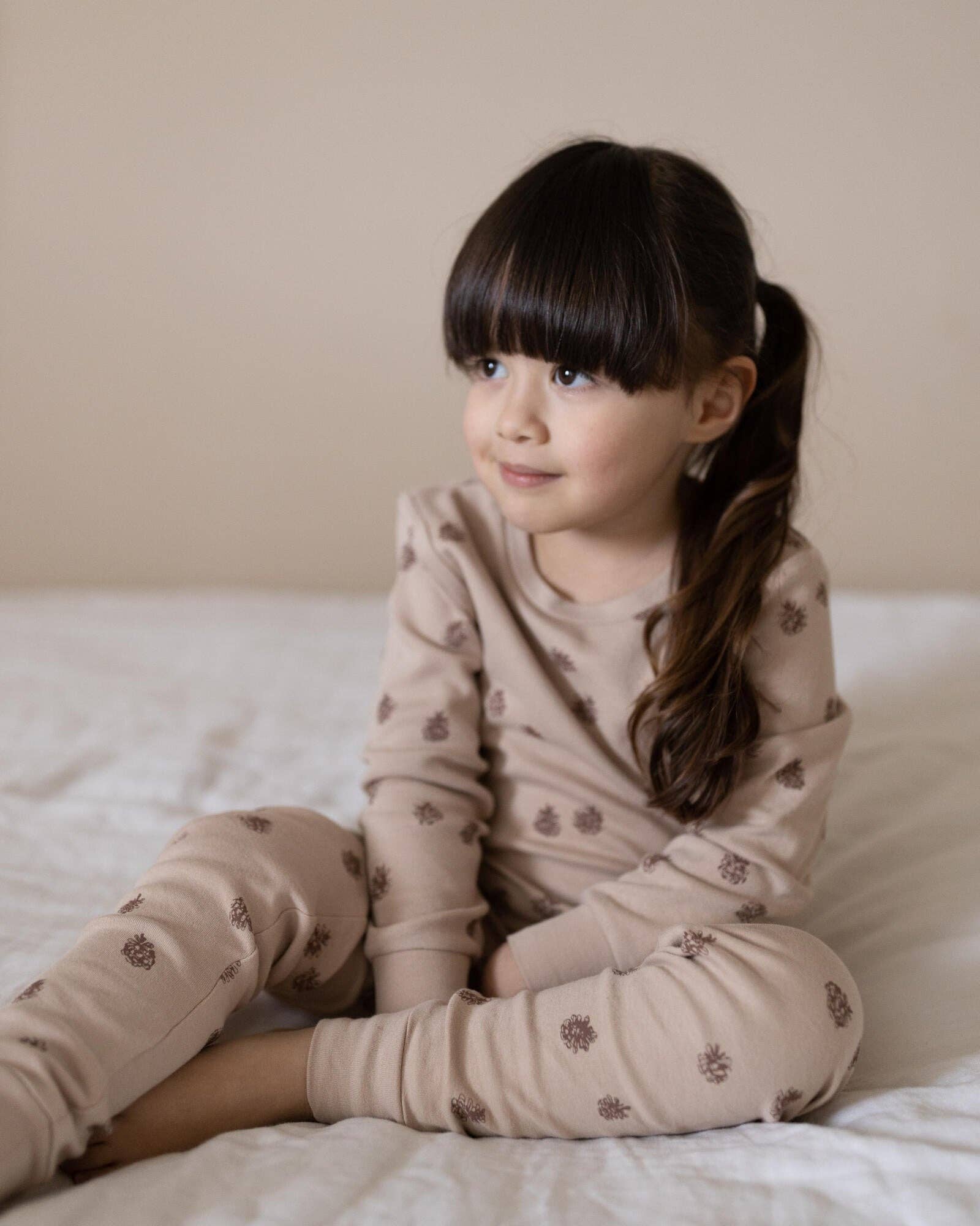 Young child in pinecones pajamas sitting on a bed with a neutral background