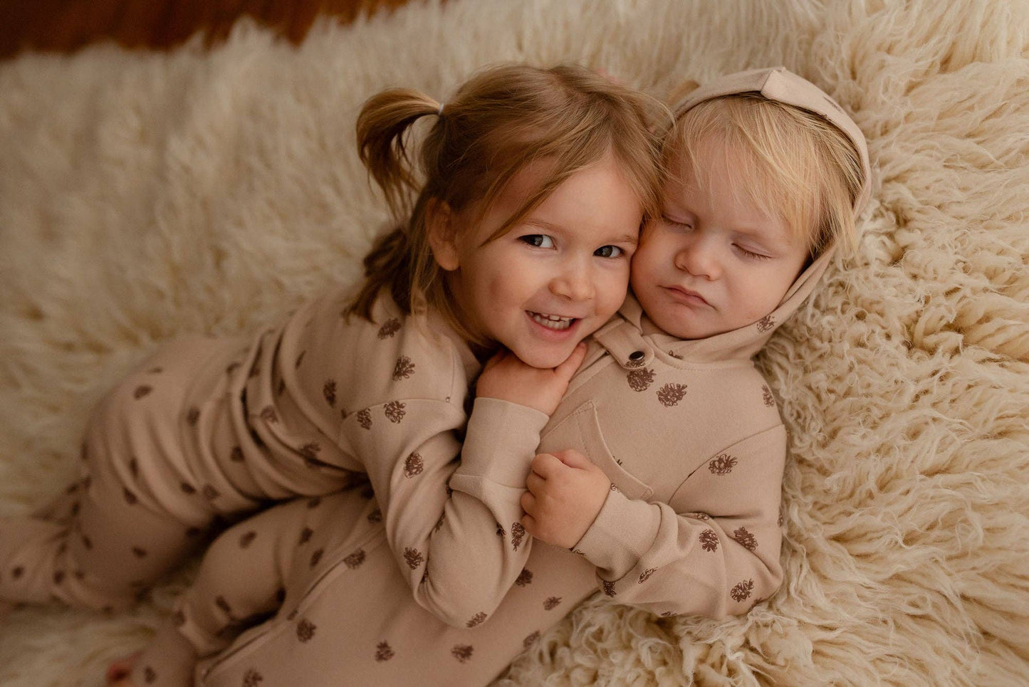 Two children in matching pajamas lying on a fluffy white surface.