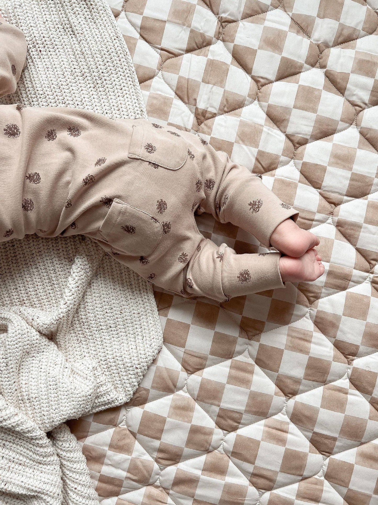 Back pockets detail for pinecones romper on a checkered bed with a textured blanket