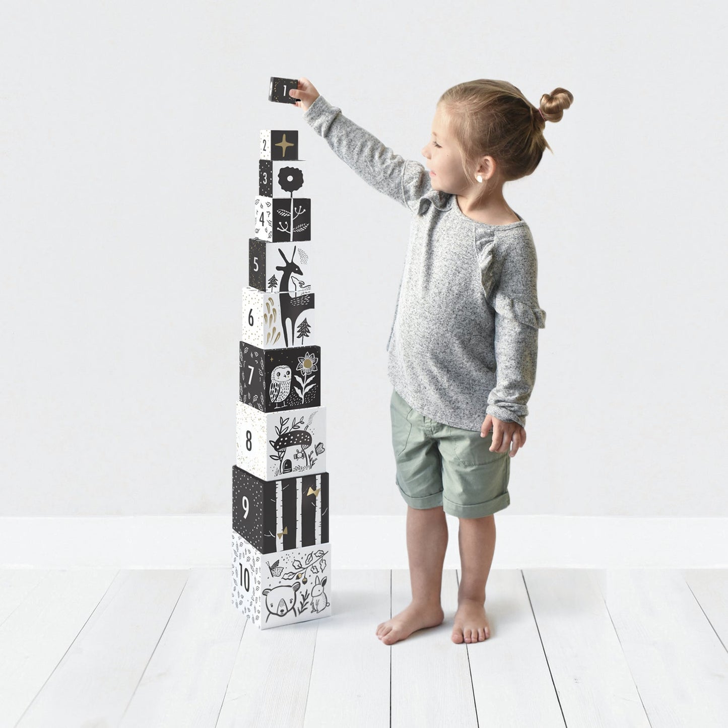 Child playing with a tower of black and white blocks on a white floor.