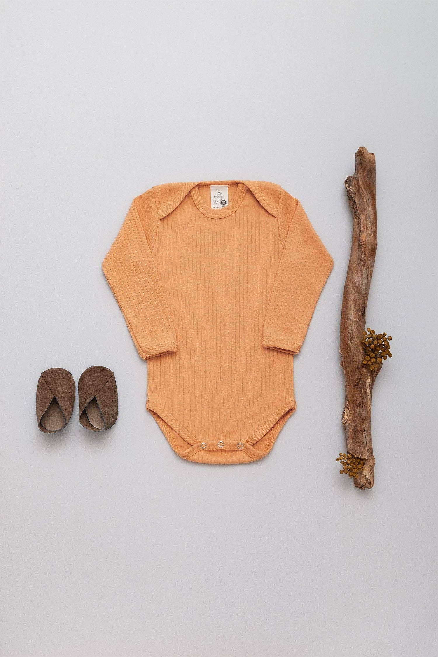 long sleeve ribbed onesie in ochre laid flat next to a stick and a pair of baby shoes