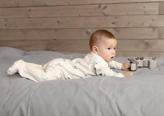 Baby laying on a bed playing with a toy train wearing a plants delight organic footie