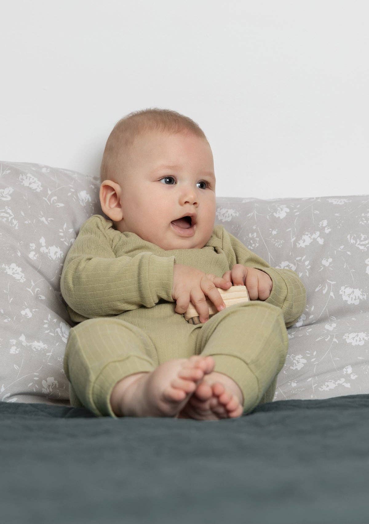 Baby sitting on a bed wearing a long sleeve sage romper