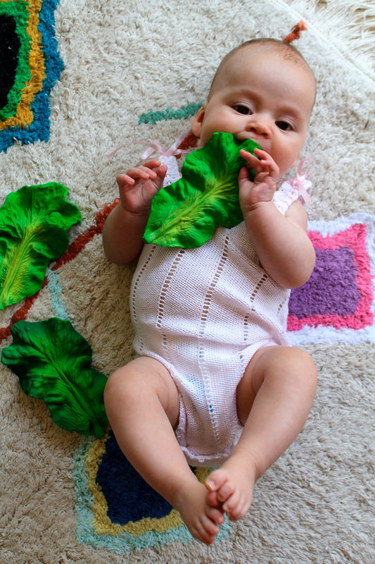 a baby laying on a rug teething on a natural rubber kale toy