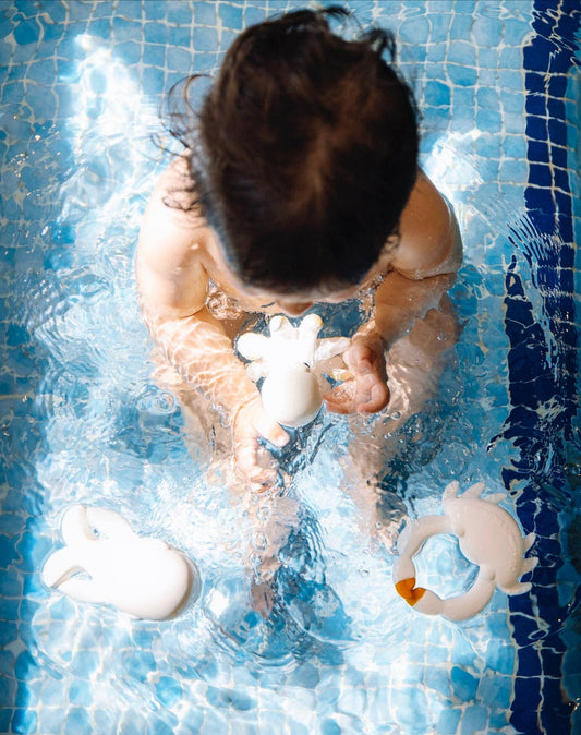 a baby sitting in water taking a bath while playing with a natural rubber octopus