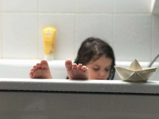 a child taking a bath with a natural rubber origami boat on the side of the tub