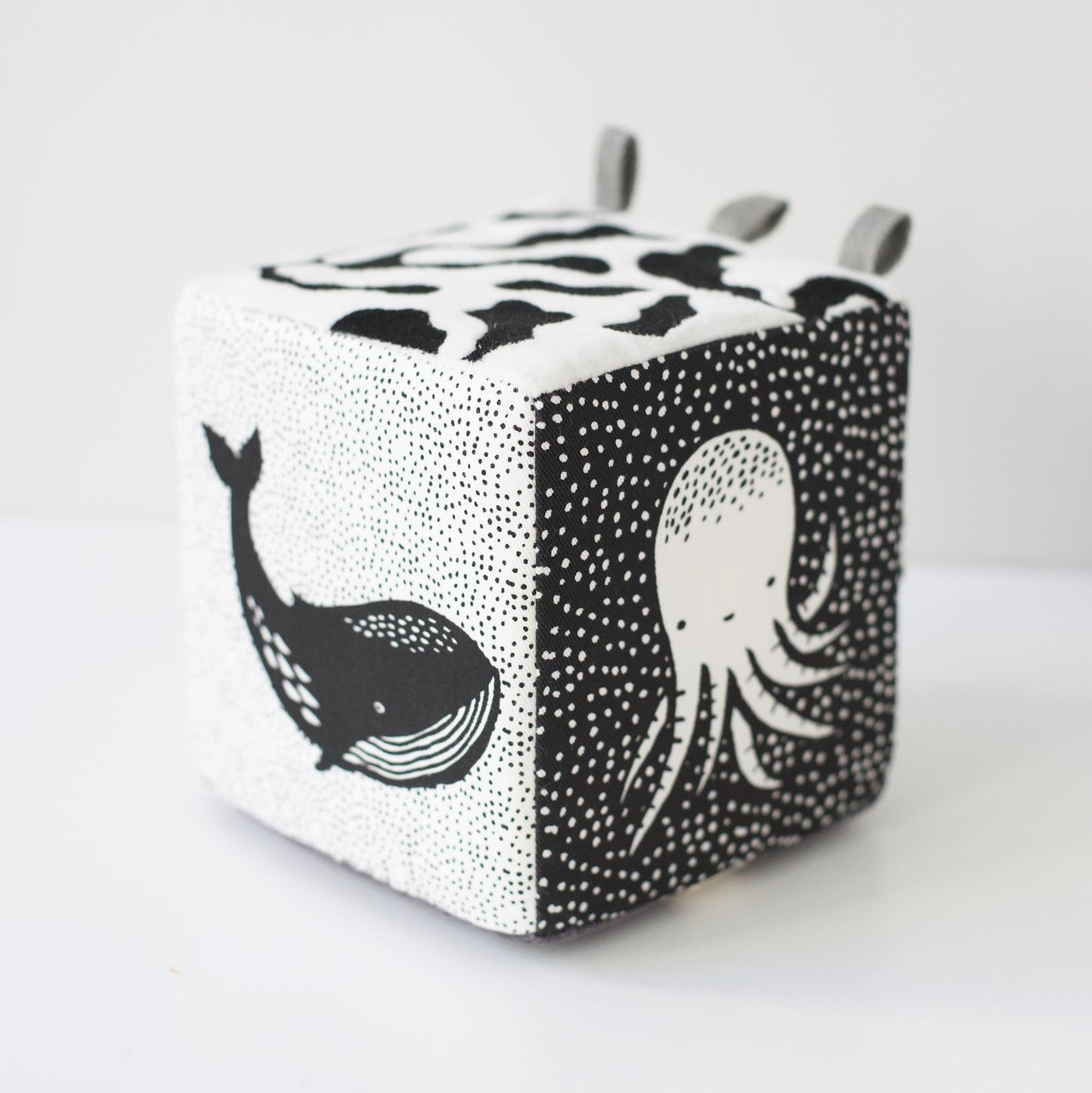 Cube-shaped block with black and white whale and octopus designs on a light gray background