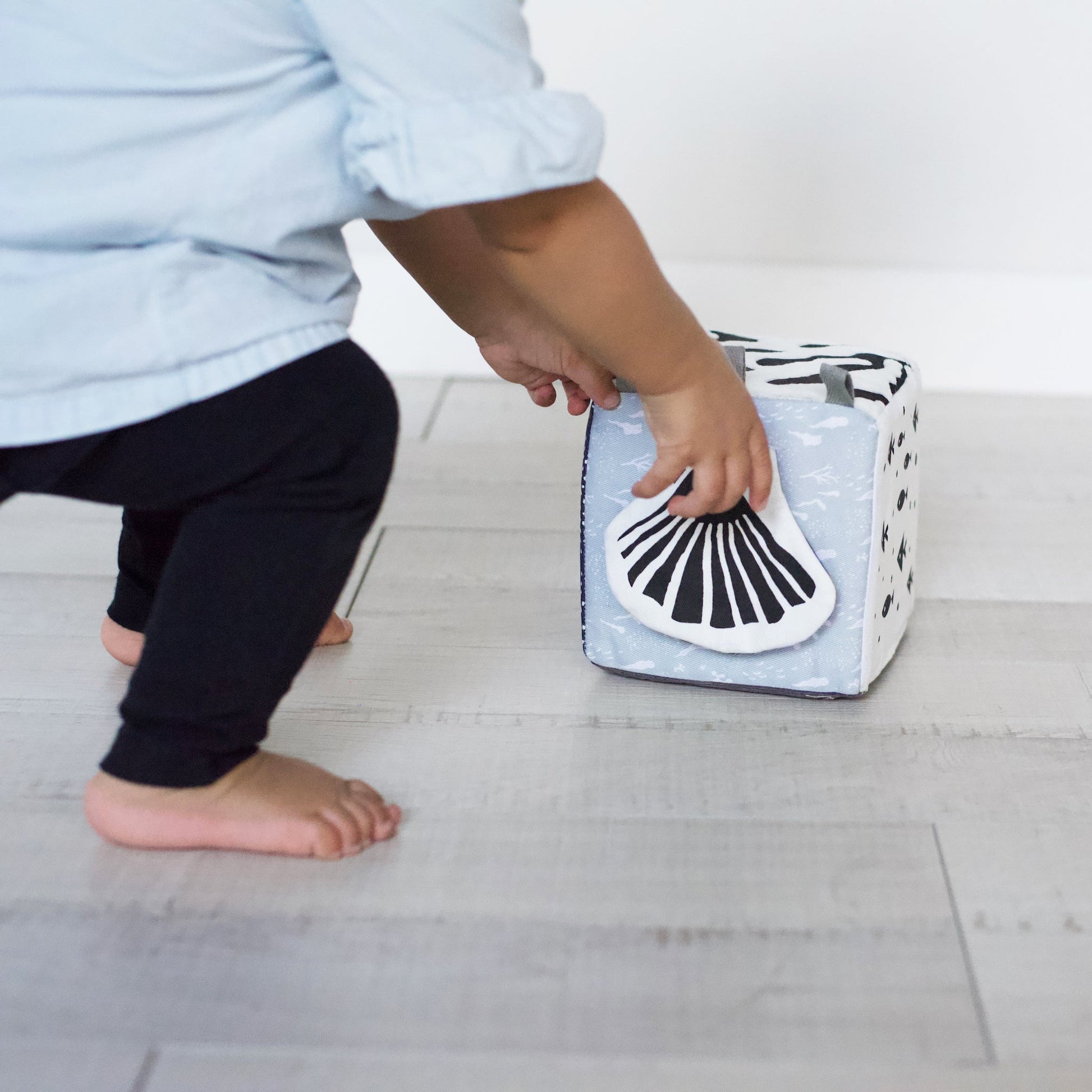 Child holding a small laundry basket with a whale design on a light wooden floor.