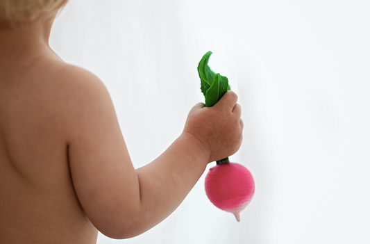 a baby with their back turned to the camera holding a natural rubber radish toy