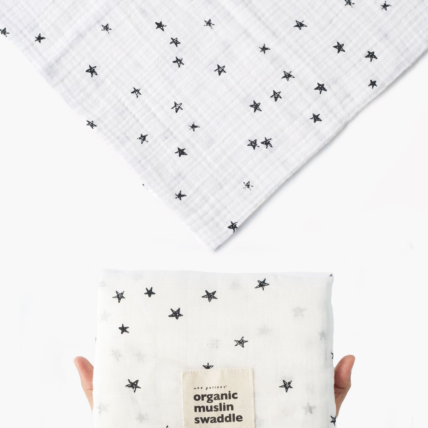 White organic muslin swaddle with black star pattern held by a hand on a white background