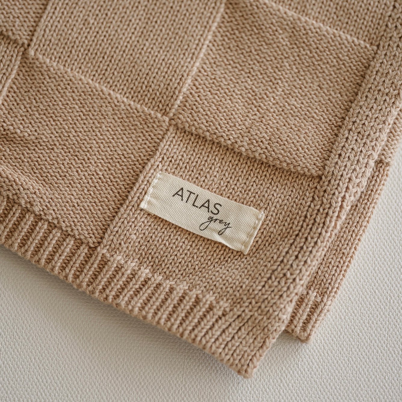 Close-up of a beige knitted fabric with a 'Atlas Grey' label on a light background