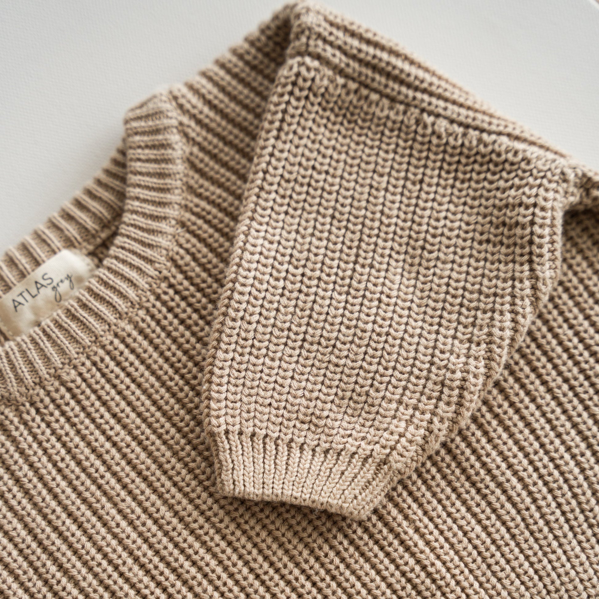 Close-up of a beige knit sweater with a brand label on a light background