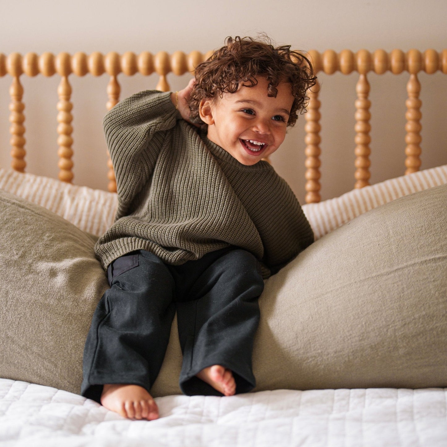 Child sitting on a bed with a wooden headboard, smiling.